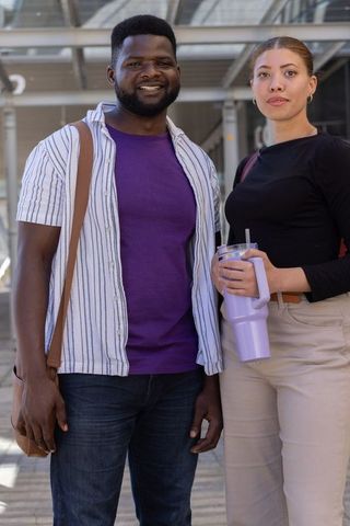 Urban commuter duo smiling and holding lavender tumbler under transit canopy