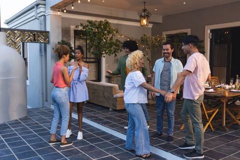 Friends celebrating on cozy patio under string lights holding hands and laughing together