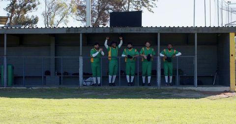 Multicultural baseball team standing in dugout celebrating in green uniforms