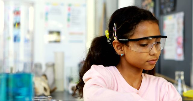 A young girl of Middle Eastern ethnicity is focused on an experiment in a science laboratory, with copy space. Her protective goggles suggest a practical learning environment where safety is a priority.