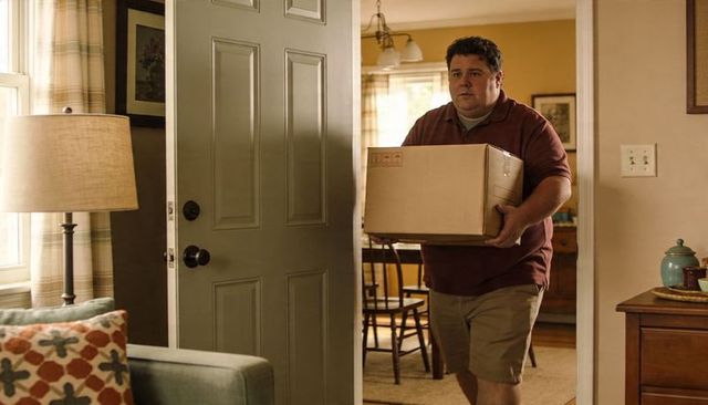 Man carrying moving box through front door into cozy home interior, casual moving day