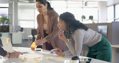 Multiracial professional women brainstorming around table in modern open office workspace