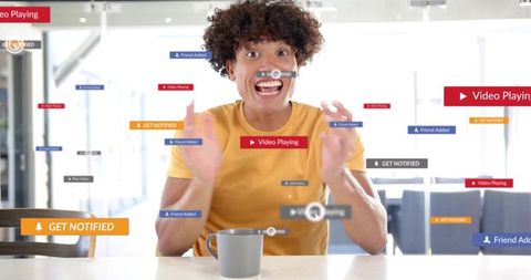 Excited curly-haired man reacting to augmented reality social media notifications in cafe