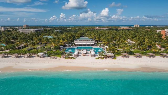 Resort pool club stretching along turquoise beach with cabanas, daybeds, palm trees