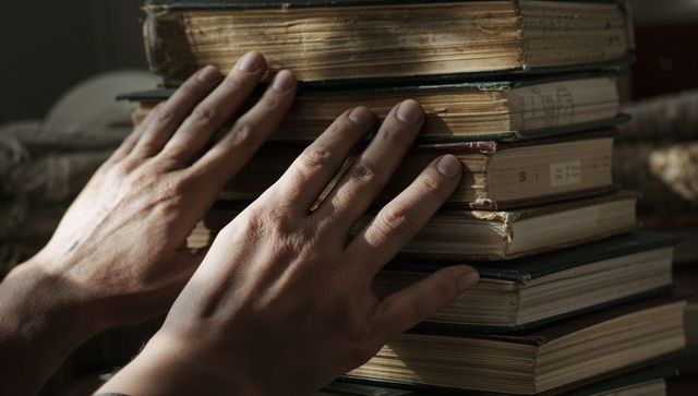 Hands Touching Stack of Worn Hardcover Library Volumes with Aged Pages and Warm Light