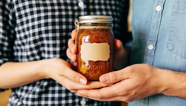 Couple holding mason jar of homemade chutney with kraft label and twine, rustic canning