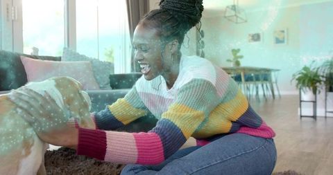 Woman joyfully petting dog on plush rug in sunlit living room wearing colorful sweater
