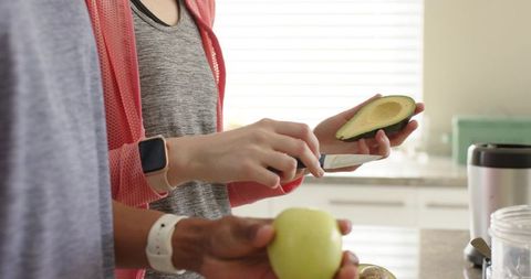 Couple slicing avocado and holding apple in bright modern kitchen with blender