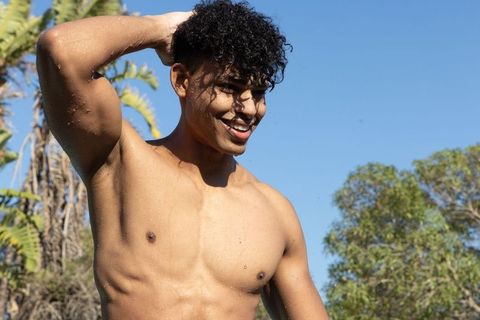 Sunlit african american man standing shirtless in tropical garden showing water droplets