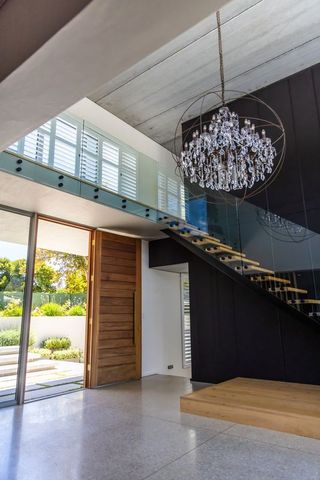 Modern foyer with floating staircase, glass balustrade, pivot wood door and chandelier