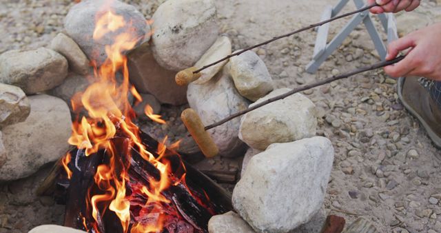 Hands of caucasian man grilling sausages in fire camping in nature with copy space. Nature, travel, tranquility, lifestyle concept, unaltered.