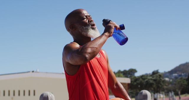 Senior african american man with basketball drinking water on the court near the beach. elderly healthy people lifestyle and sport concept