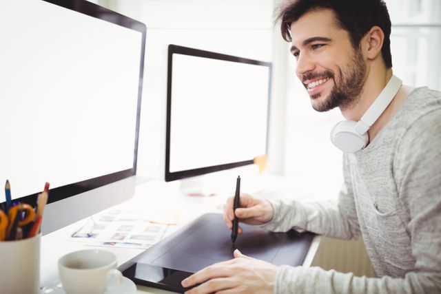 Smiling businessman using graphics tablet in front of computers in creative office
