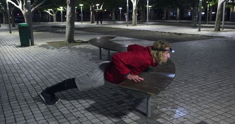 Man with headlamp doing evening pushups on bench in city park