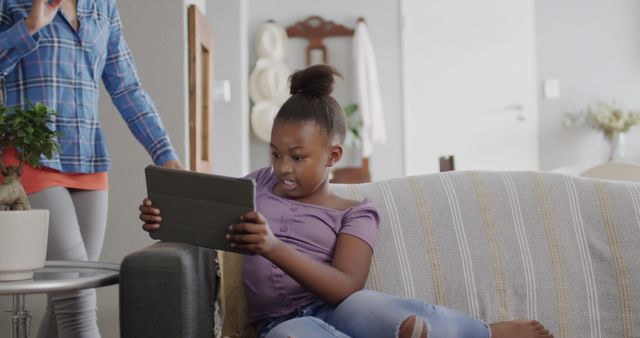 Young girl using tablet on couch at home with mother - Download Free Stock Images Pikwizard.com