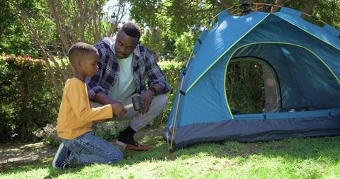 African american father teaching son setting up backyard tent during camping weekend