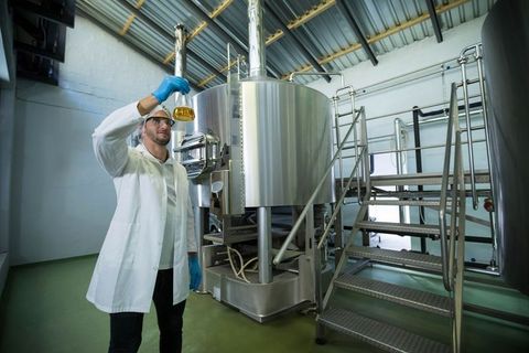 Scientist Examining Liquid in Brewery Facility with Steel Tank Backdrop
