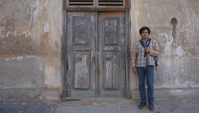 Man standing by weathered wooden door on urban street with vintage facade and copy space