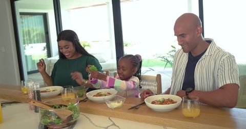 Sunlit modern kitchen family sharing pasta and salad, multiethnic family enjoying meal