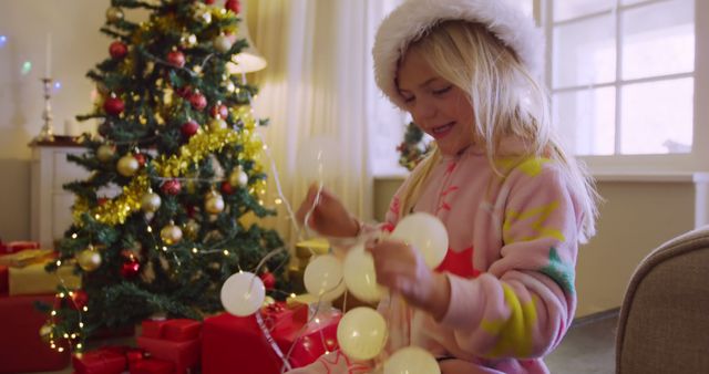 Caucasian girl decorates a Christmas tree at home. She's immersed in the holiday spirit, arranging festive ornaments with care.