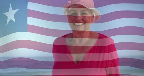 Smiling senior woman wearing sunhat standing on beach with american flag overlay