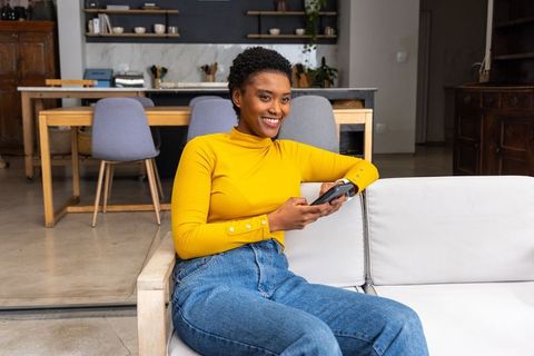 Smiling african american woman relaxing on sofa in modern minimalist open-concept home