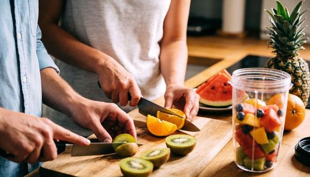 Couple chopping fresh fruit for smoothie on wooden cutting board with chef knives