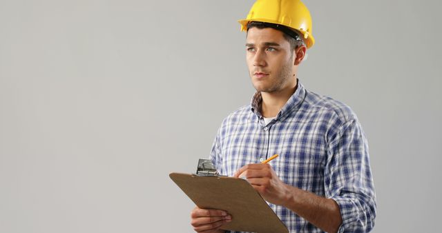 A young Caucasian man wearing a hard hat holds a clipboard, with copy space. His attire and equipment suggest he is a professional in the construction or engineering industry.