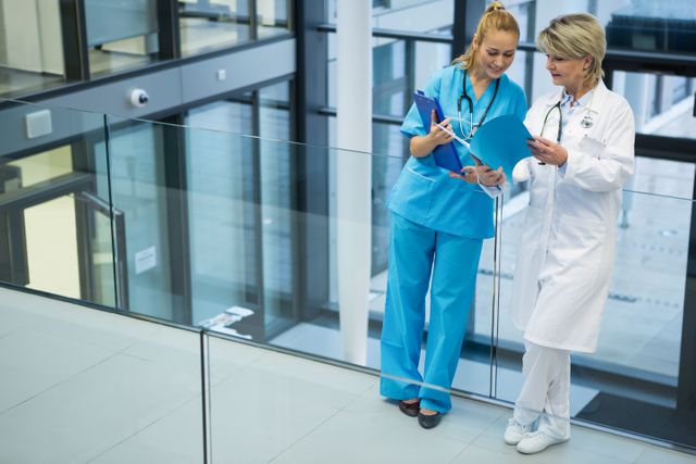 Female doctor and nurse standing in a modern hospital, reviewing a medical report together. This image can be used for healthcare-related articles, medical websites, hospital brochures, and educational materials about teamwork and collaboration in healthcare settings.