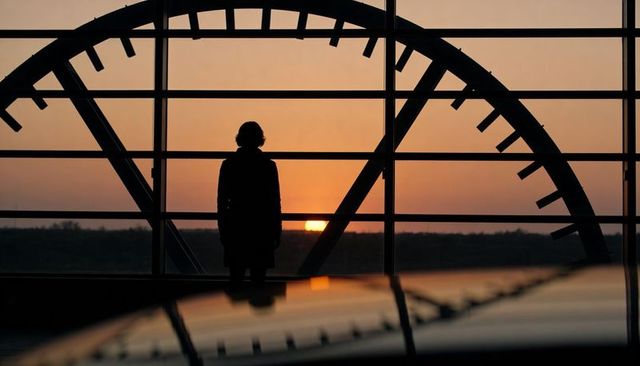 Silhouette standing inside large clock window watching sunset with reflective floor horizon