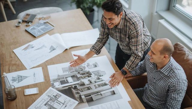 Architects collaborating over large building renderings on wooden table in modern studio