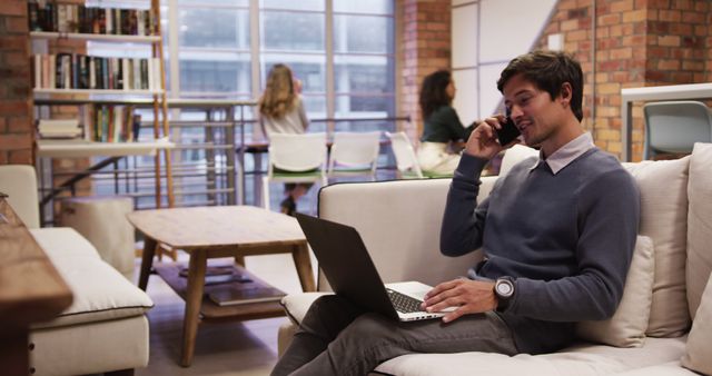 Young Professional Talking on Phone While Working on Laptop in Modern Office Lounge - Download Free Stock Images Pikwizard.com