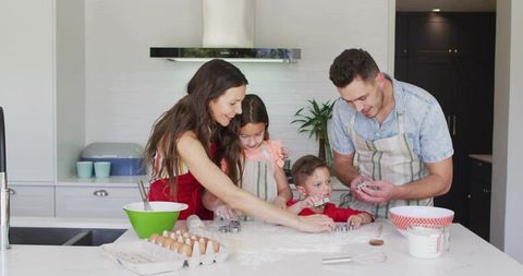 Family of four baking together on kitchen island using cookie cutters and mixing dough