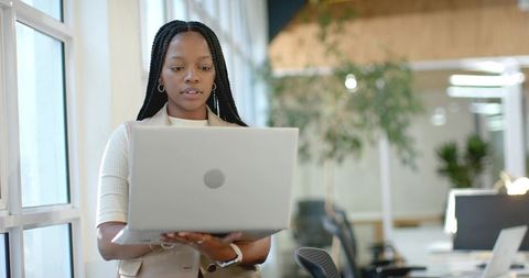 African American professional holding laptop and working in bright modern open-plan office