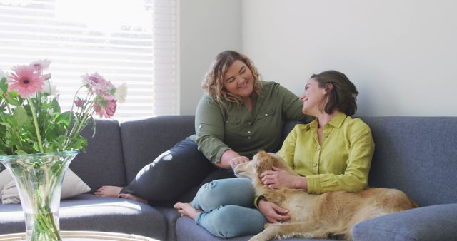Caucasian lesbian couple smiling and sitting on couch with dog. domestic life, spending free time relaxing at home.