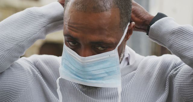Man adjusting face mask, ensuring proper fit for outdoor safety. Ideal for use in health and safety campaigns, educational materials about COVID-19 precautions, or articles related to public health.