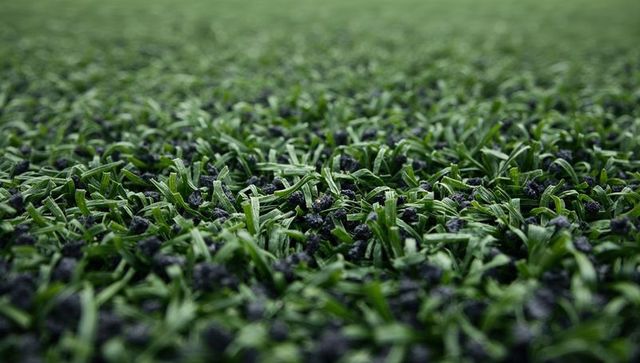 Macro close-up of artificial turf with rubber infill granules and lifelike fiber texture