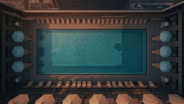 Symmetrical rooftop pool courtyard at golden hour with loungers, umbrellas, modern geometry