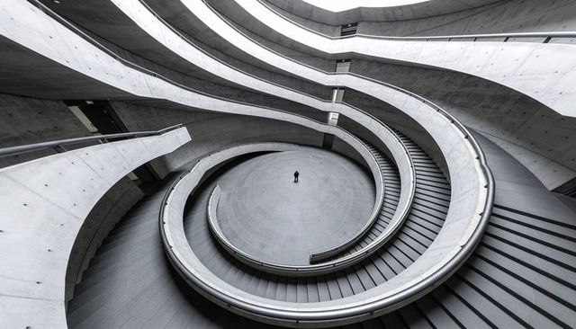 Solitary figure standing at center of spiral concrete atrium with sweeping ramps