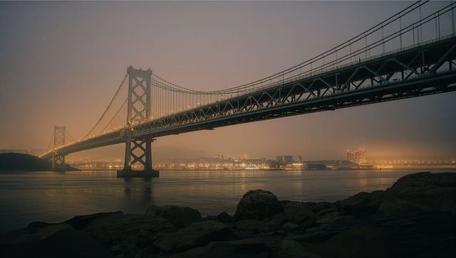 Illuminated Suspension Bridge at Dusk with City Skyline