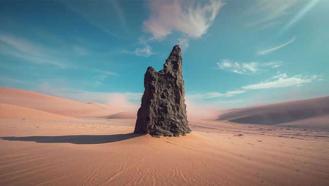 Majestic Rock Spire in Sunlit Desert with Unique Dune Formations