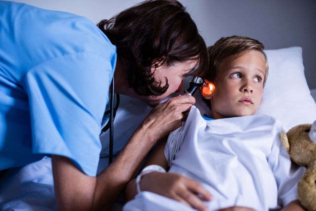 This image depicts a female doctor using an otoscope to examine a child's ear in a hospital setting. The child is lying on a bed, looking slightly concerned. This image can be used for healthcare-related content, pediatric care articles, medical websites, or educational materials about ear examinations and child healthcare.