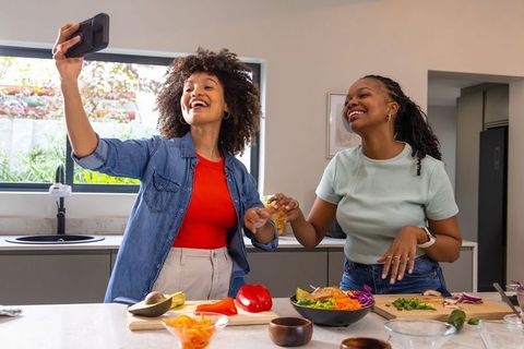 Two friends taking selfie while preparing vibrant salad at kitchen island capturing joy