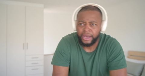 Surprised man reacting while wearing headphones and leaning forward in minimalist bedroom