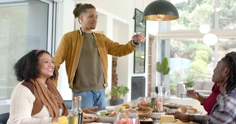 Diverse Friends Raising Glasses Over Casual Home Dinner with Salads, Bread, Cozy Interior
