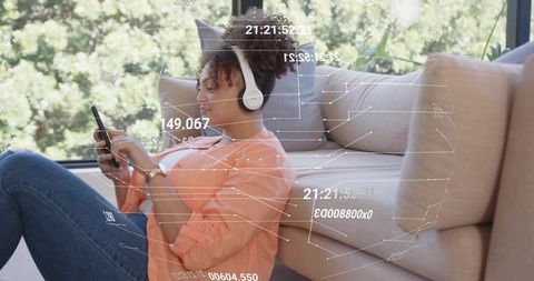 Using smartphone and headphones while relaxing on sofa with futuristic data overlay