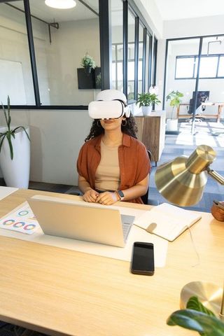 Exploring virtual workspace wearing white vr headset at modern office desk with laptop