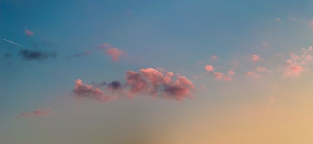 Golden hour sky with scattered pink clouds illuminated by setting sun, showcasing peaceful and calming atmosphere. Ideal for use in backgrounds, nature-themed articles, desktop wallpapers, relaxation-inspired projects, or environment-related marketing materials.