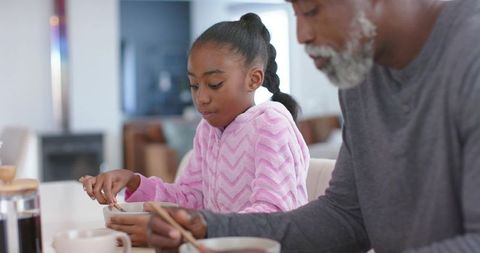 African american man and teen girl stirring breakfast together in cozy morning kitchen