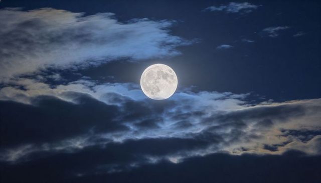 Full Moon Emerging Through Layered Clouds with Luminous Halo and Starry Night Sky